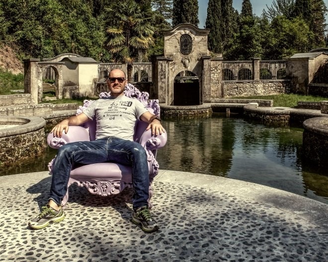 Italian man sitting on a throne beside a pond in a villa near Lake Garda.